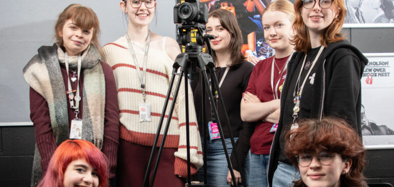 A Level Film Studies students filming in front of classroom posters