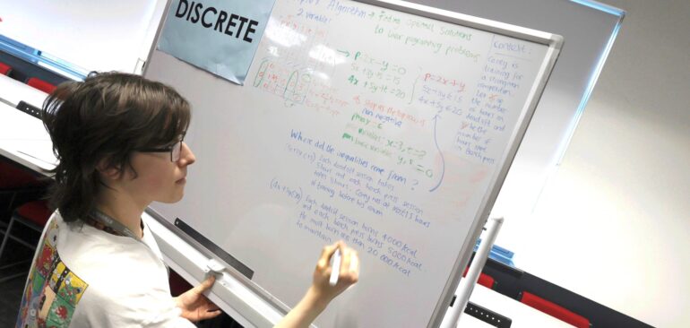 A Level Further Maths student writing equations on whiteboard in classroom